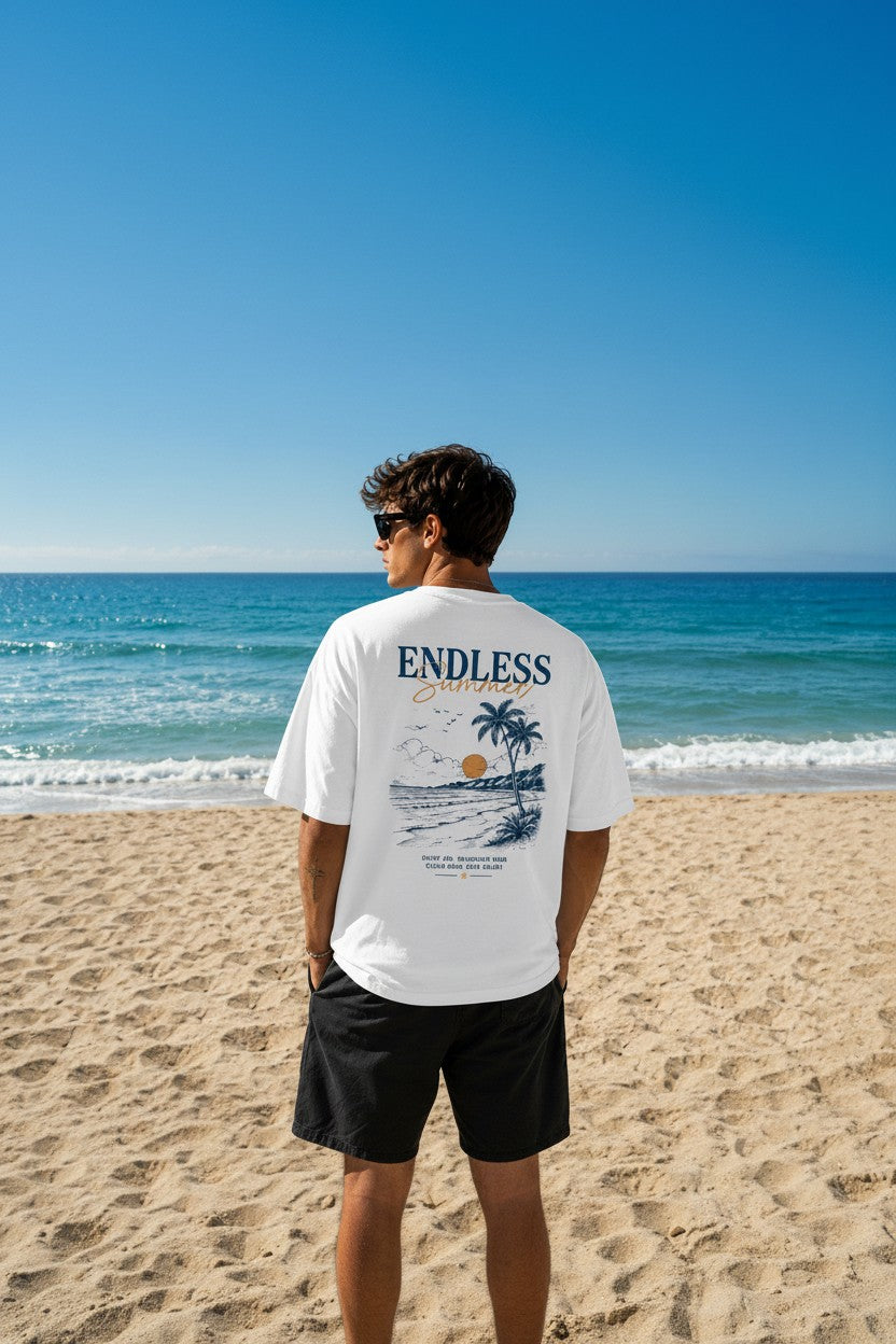 CrowsGate beyaz oversize tişört, sırtında plaj temalı Endless Summer baskısı ile sahilde duran erkek model.